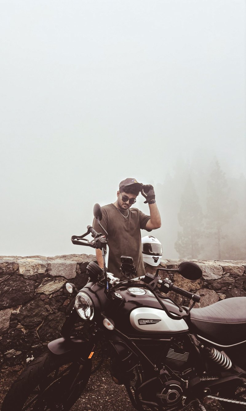 Pratik Parashar standing beside a Ducati Scrambler on a fog-covered mountain road